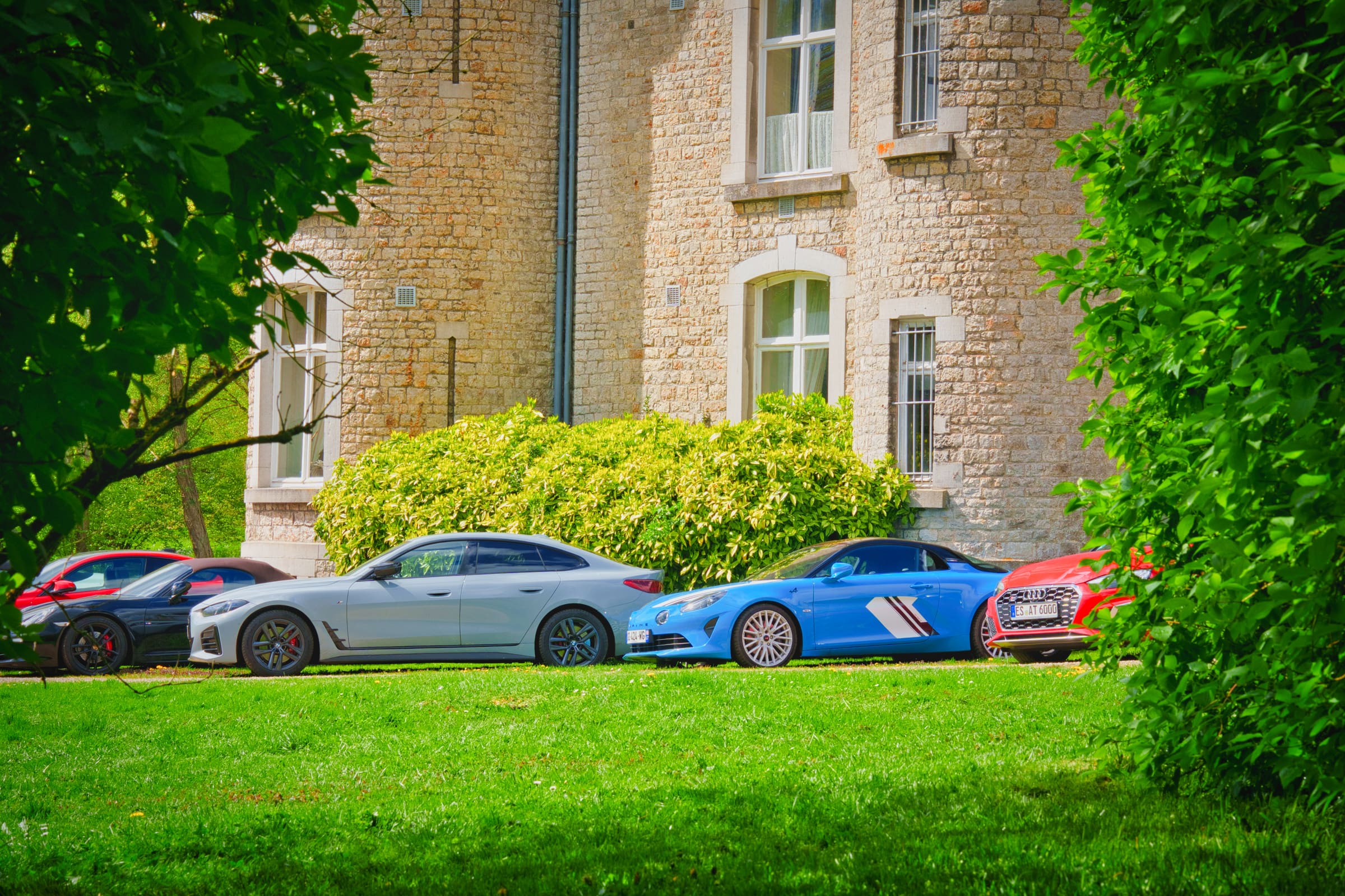 Façade en pierre d'un château avec voitures garées sur la pelouse