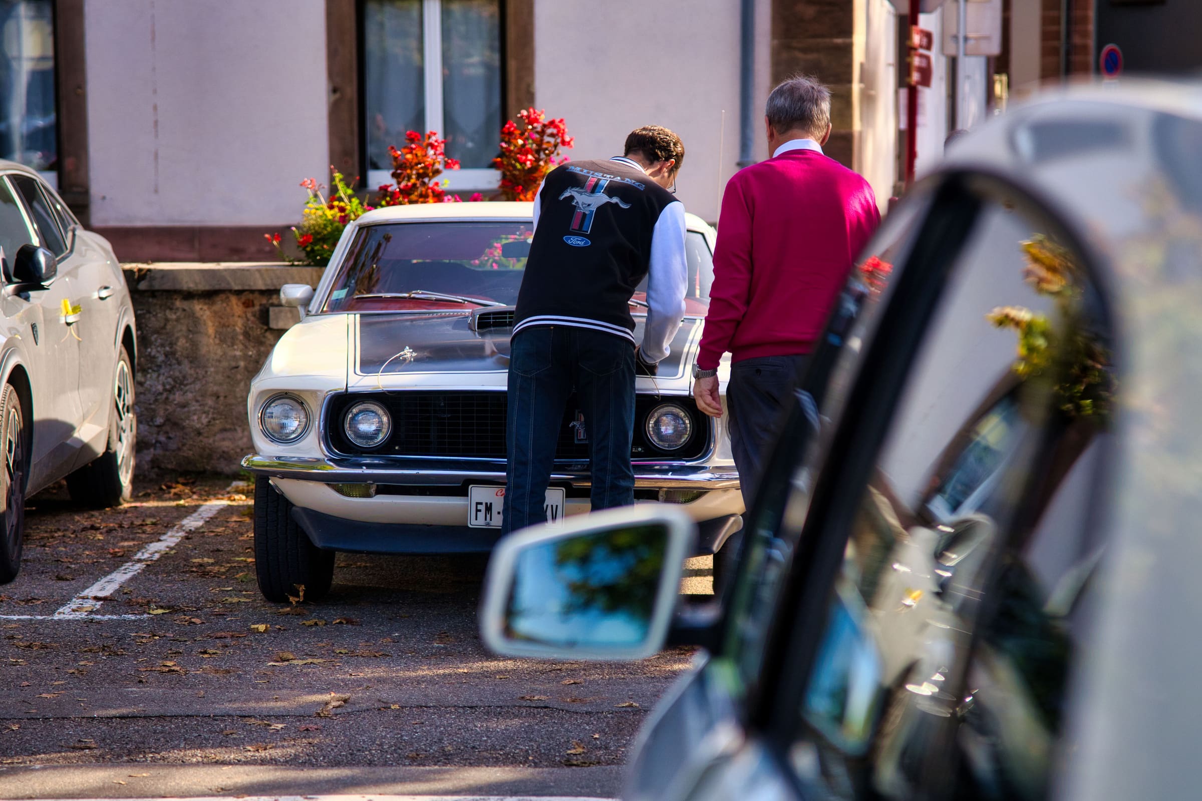 Ford Mustang de collection blanche examinée par deux passionnés dans la rue
